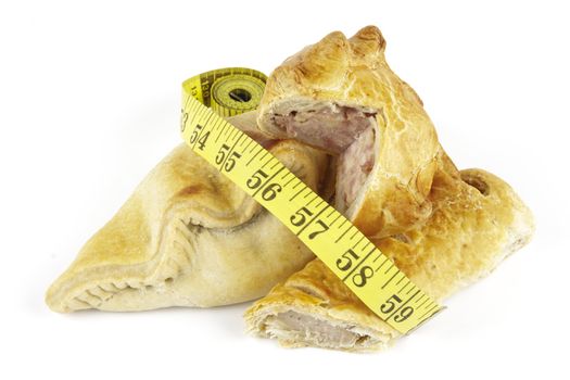 Single golden sausage roll cut in half with pork pie and pasty with a yellow tape measure on a reflective white background