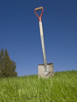 Shovel in green grass against a blue sky