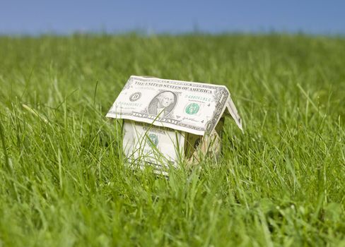 A miniature house made of dollar bills outside in the grass.