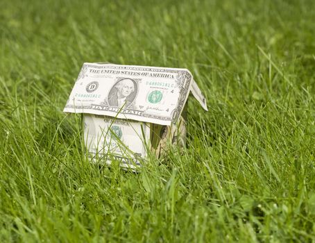 A miniature house made of dollar bills outside in the grass.