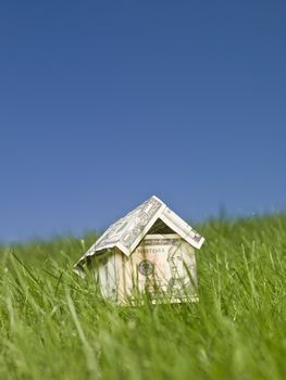 A miniature house made of dollar bills outside in the grass.