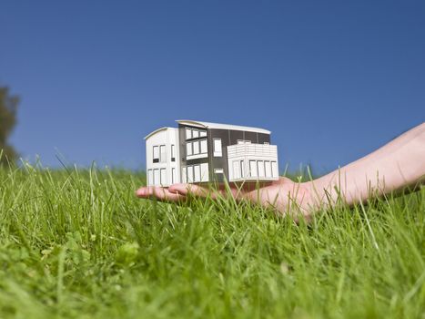 Man holding a miniature house outside in the sun.