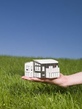 Man holding a miniature house outside in the sun.