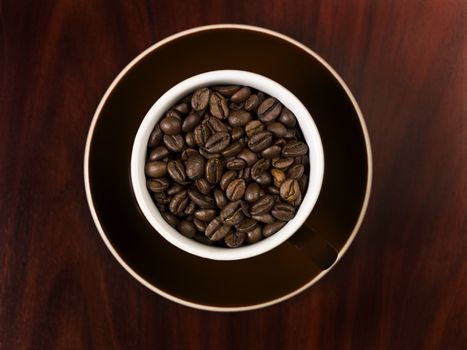 High angle view of coffee beans in a cup with a wooden background.