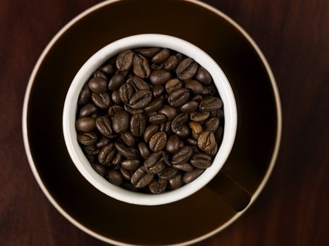 High angle view of coffee beans in a cup with a wooden background.