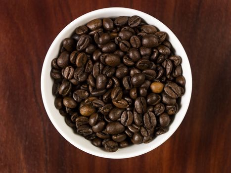 High angle view of coffee beans in a cup with a wooden background.