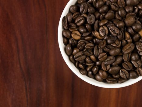 High angle view of coffee beans in a cup with a wooden background.
