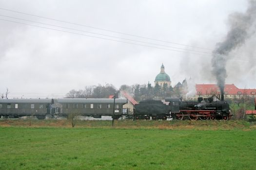 Old retro steam train passing the fields with a palace in background
