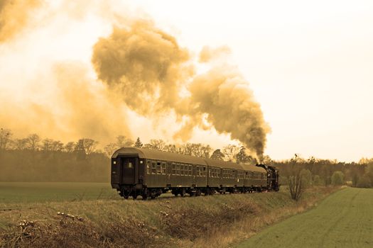 Steam retro train running through the countryside with lot of smoke over the sky
