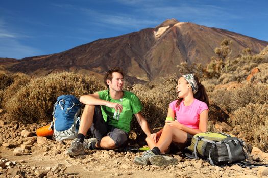 People hiking. Young beautiful couple taking a break, relaxing and eating during a hike / backpacking trip in the beautiful and wild volcanic landscape in the national park on the volcano, Teide, Tenerife, Spain. 