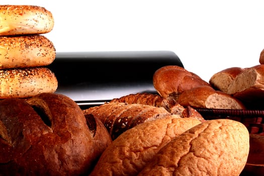 Rolls and bread of the different form and colour, against a wooden table and a bread bin.