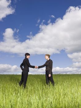 Two women standing in the grass shaking hands