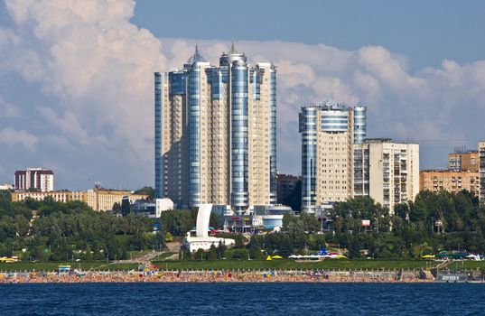 High apartment buildings on the quay. Beach filled with people. Summer urban landscape with a river. Samara. Russia.