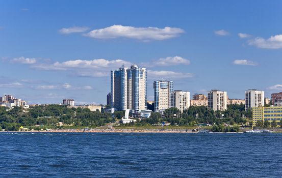 High apartment buildings on the quay. Beach filled with people. Summer urban landscape with a river. Samara. Russia.