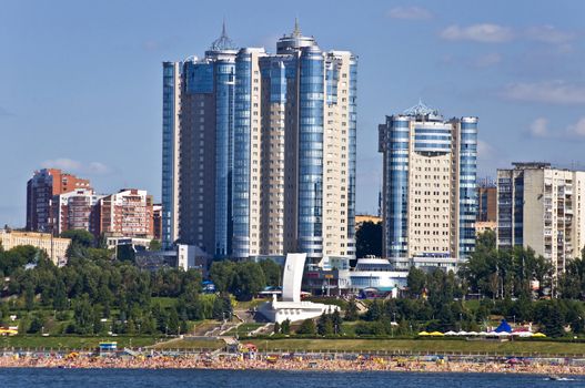 High apartment buildings on the quay. Beach filled with people. Summer urban landscape with a river. Samara. Russia.