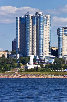 High apartment buildings on the quay. Beach filled with people. Summer urban landscape with a river. Samara. Russia.