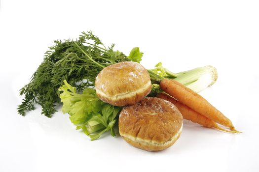 Contradiction between healthy food and junk food using a bunch of carrots and celery with two doughnuts on a reflective white background 