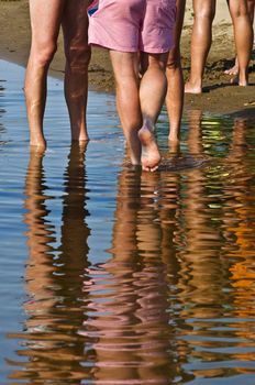 Men's feet are on the water at the beach. Reflection and ripples in the water. Summer.