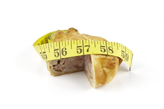 Single golden pork pie and yellow tape measure on a reflective white background