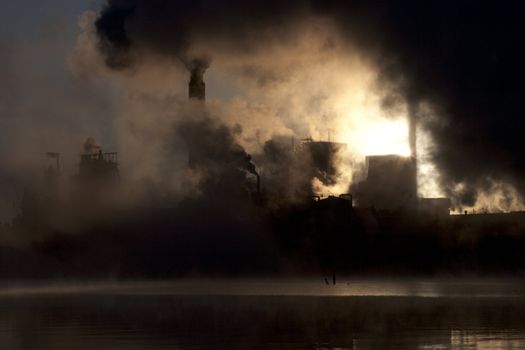 Paper mill covered by heavy smoke screen by hazy sunrise.