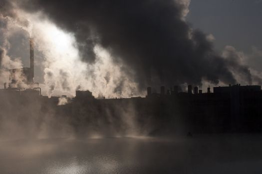 Paper mill covered by heavy smoke screen by hazy sunrise.