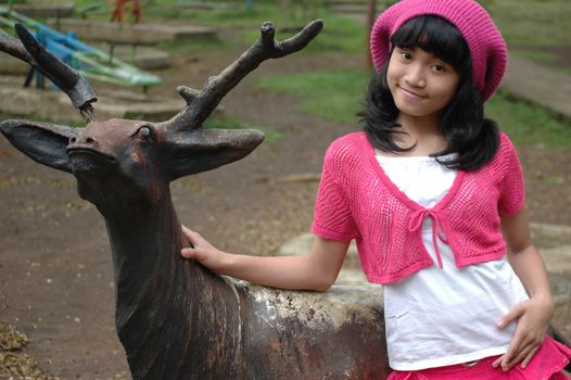 cute girl stand up beside dear statue in park
