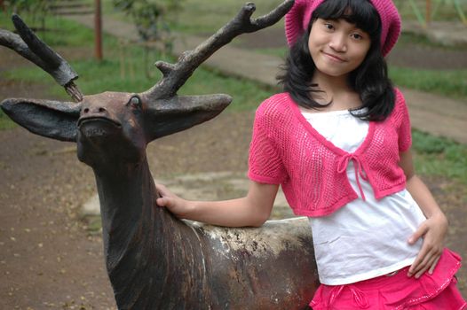 cute girl stand up beside dear statue in park
