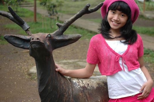 cute girl stand up beside dear statue in park