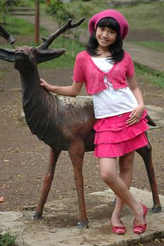 cute girl stand up beside dear statue in park