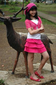 cute girl stand up beside dear statue in park