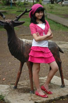 cute girl stand up beside dear statue in park