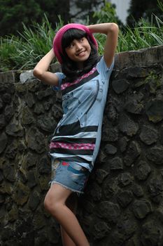 cute asian girl stand up beside rock wall in park