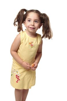 Cute toddler girl with natural wavy hair pulled into ponytails.  She is wearing a yellow outfit with embroidery and is holding a lollipop candy on a stick.