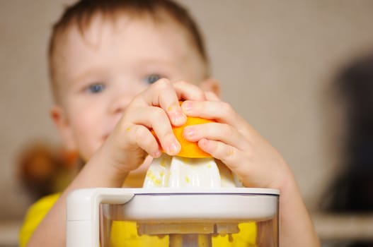 The child in a yellow vest to wring out juice  from an orange