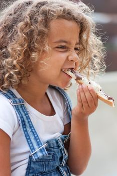 Girl crunching heartily into a slice of bread with chocolate