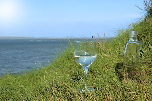 single glass and bottle of pure natural water standing on the beach dunes in kerry ireland
