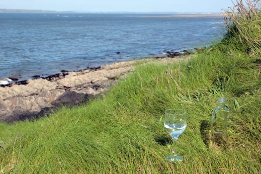 single glass and bottle of pure natural water standing on the beach dunes in kerry ireland