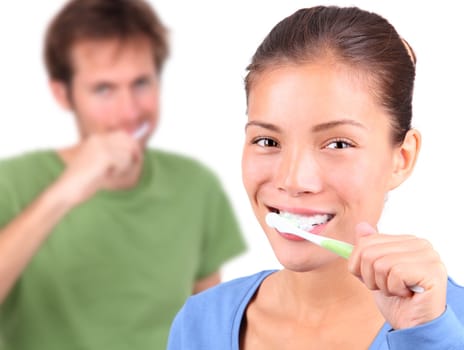 Young mixed race couple brushing teeth together on white background.