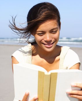 Candid image of a woman reading a book on the beach