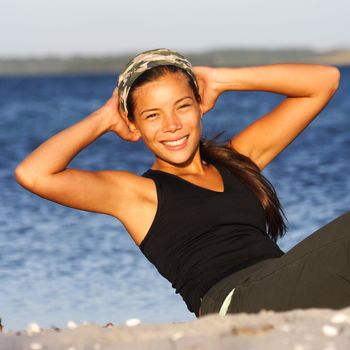 Woman doing situps / exercise outdoors on the beach with the ocean in the background