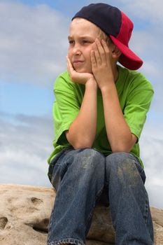 A nine year old boy on a rock looking sideways 