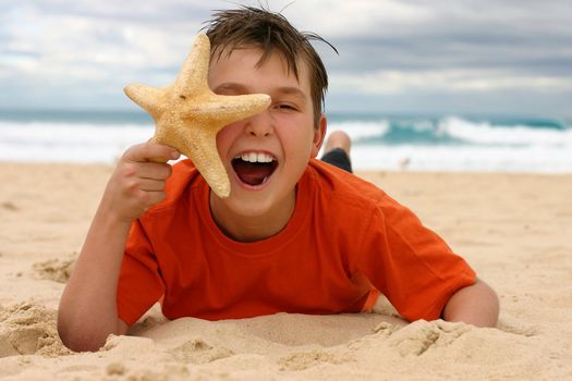 Ecstatic child lying on the beach holding a starfish to face.