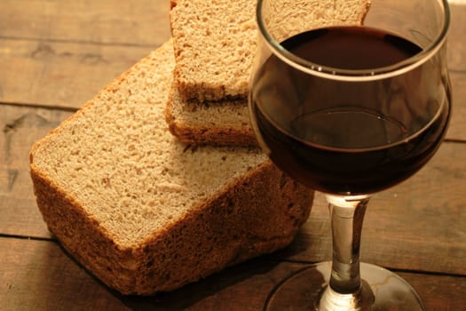 Closeup of rye bread and goblet of red wine on wooden background