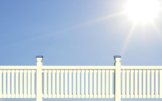 White wood picket fence against blue sky and sun