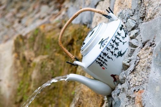 A teapot is adapted and fixed in wall at fountain