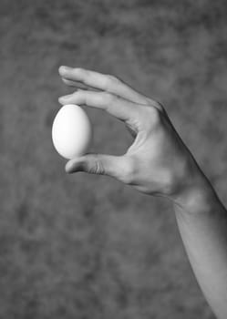 Hand holding an egg towards grey background