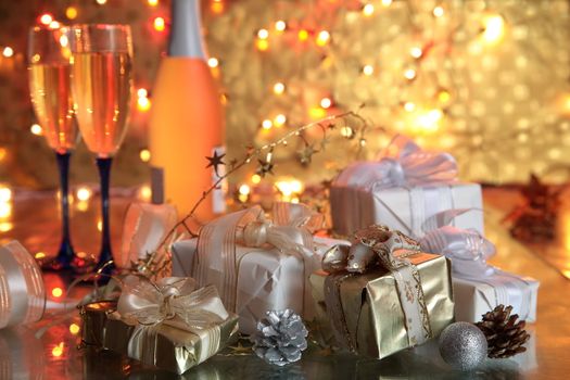 Gift boxes and glasses with champagne on golden background with blurred lights.