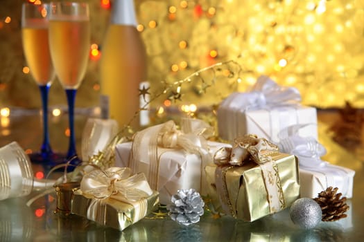 Gift boxes and glasses with champagne on golden background with blurred lights.
