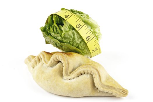 Contradiction between healthy food and junk food using a green salad lettace and pasty with a yellow tape measure on a reflective white background 