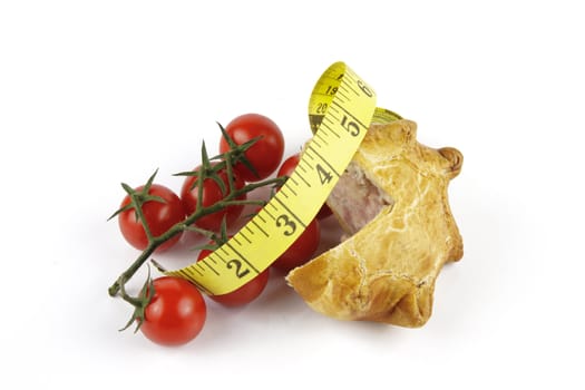 Contradiction between healthy food and junk food using tomatoes and a pork pie with a tape measure on a reflective white background 